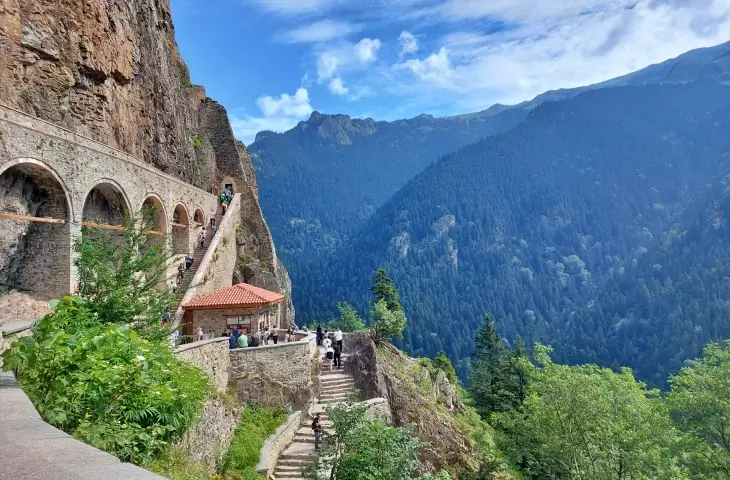 Sümela Manastırı’na çıkan tarihi taş merdivenler ve su kemeri; Altındere Vadisi’ne bakan geniş orman manzarası ve yürüyüş yapan ziyaretçiler.